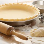 Unbaked pie crust in a metal pan, ready for making chicken pot pie, with a rolling pin and pastry cutter on a floured surface.