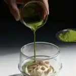 Matcha affogato being poured over vanilla ice cream in a clear glass