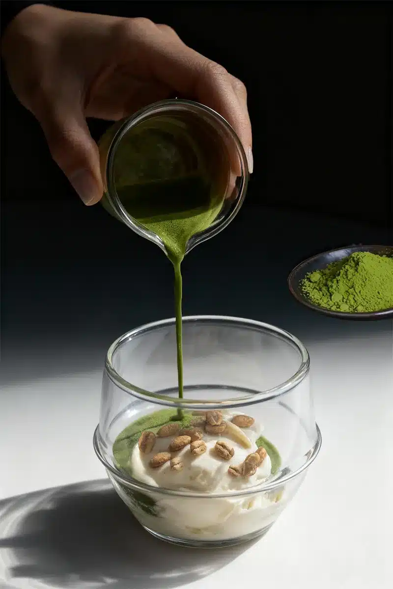 Matcha affogato being poured over vanilla ice cream in a clear glass