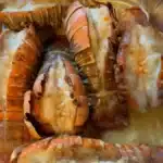 Baked lobster tails with garlic butter in a foil pan, tender lobster meat topped with melted butter