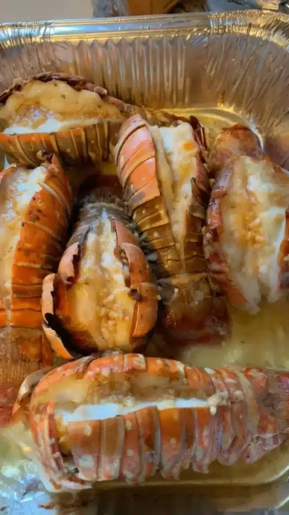 Baked lobster tails with garlic butter in a foil pan, tender lobster meat topped with melted butter