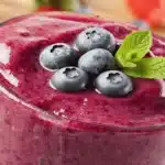 Bebida de mirtilo para saciedade: smoothie roxo com mirtilos frescos e hortelã em copo transparente.