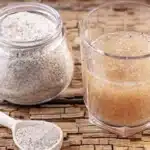 Psyllium husk powder in a jar with a spoon and a glass of psyllium fiber drink on a wooden table.