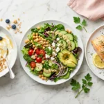 What Eric Topol Eats in a Day: Three longevity-focused meals showing Greek yogurt berry breakfast bowl, big green salad with chickpeas, and baked salmon with roasted vegetables on marble surface